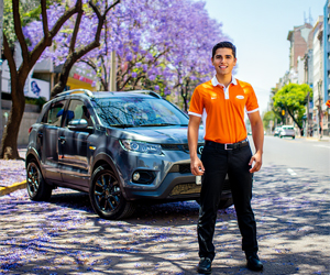 Alquiler de SUV en Buenos Aires con Diversidad Rent a Car. Empleado con uniforme naranja y blanco junto al vehículo en una calle con jacarandás en flor durante la primavera porteña.