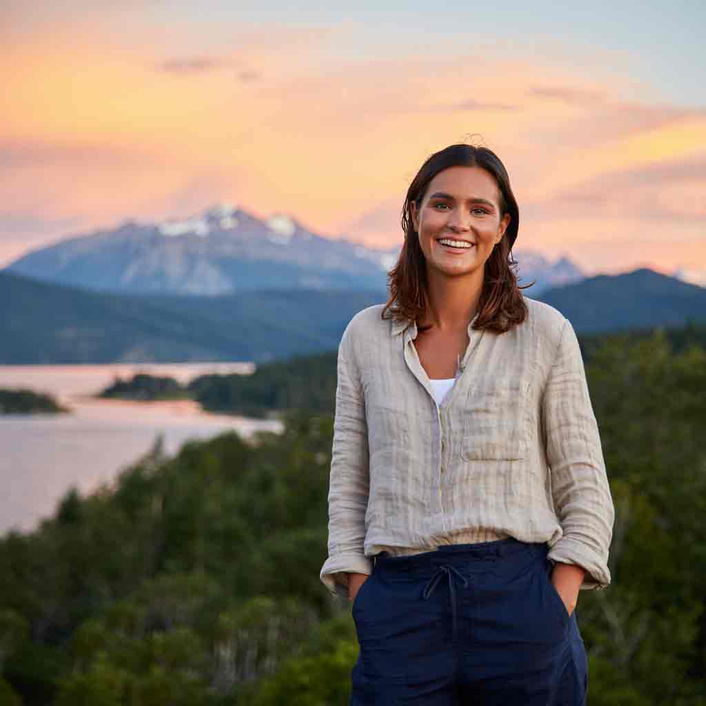 Retrato de Mariela G., viajera sonriente en Bariloche con paisaje de montañas y lago, cliente del Rent a Car de Diversidad. Turismo Activo & de Naturaleza.